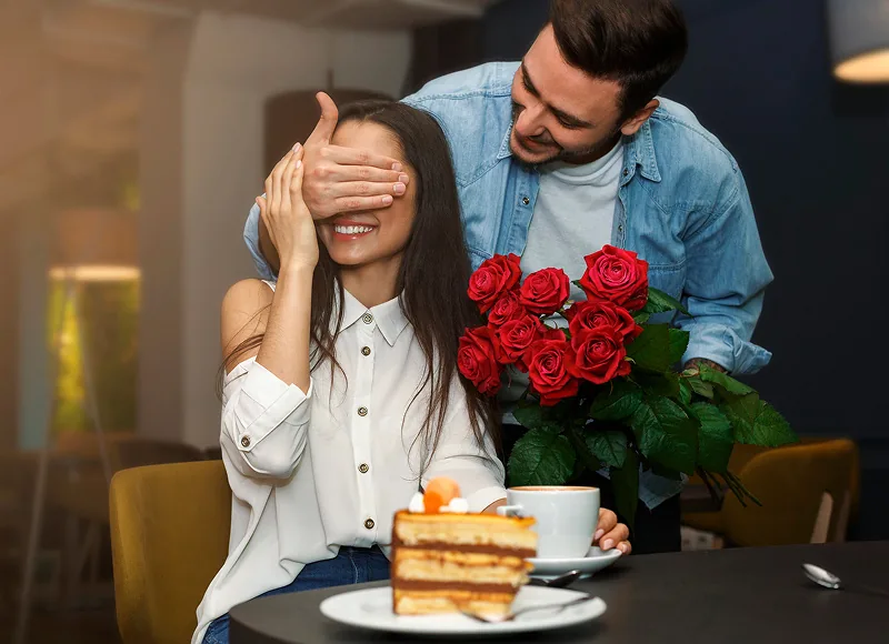 A man surprising his partner with red roses at a café
